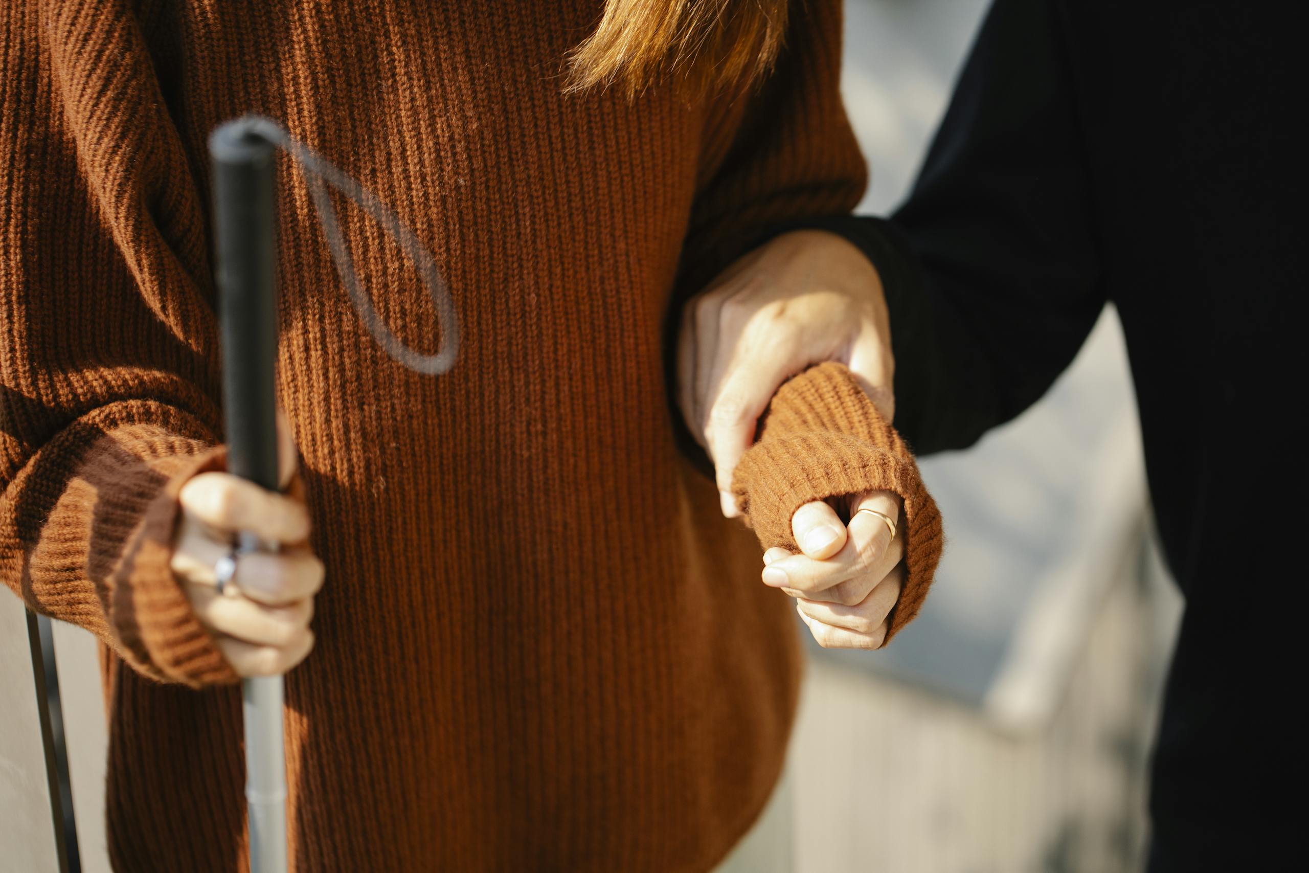 Disabilità e cecità: una ragazza tiene il bastone della cecità in mano mentre un'altra la sorregge